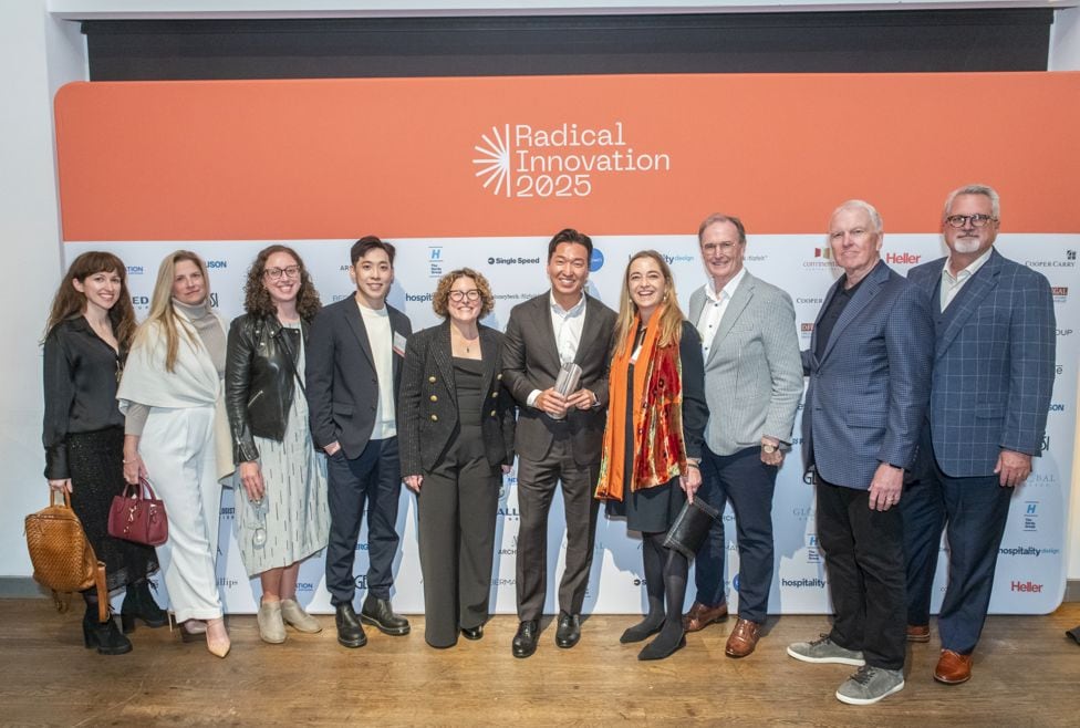 Group photo of about eleven people in formal/business attire lined up in front of the Radical Innovation 2025 backdrop at an event
