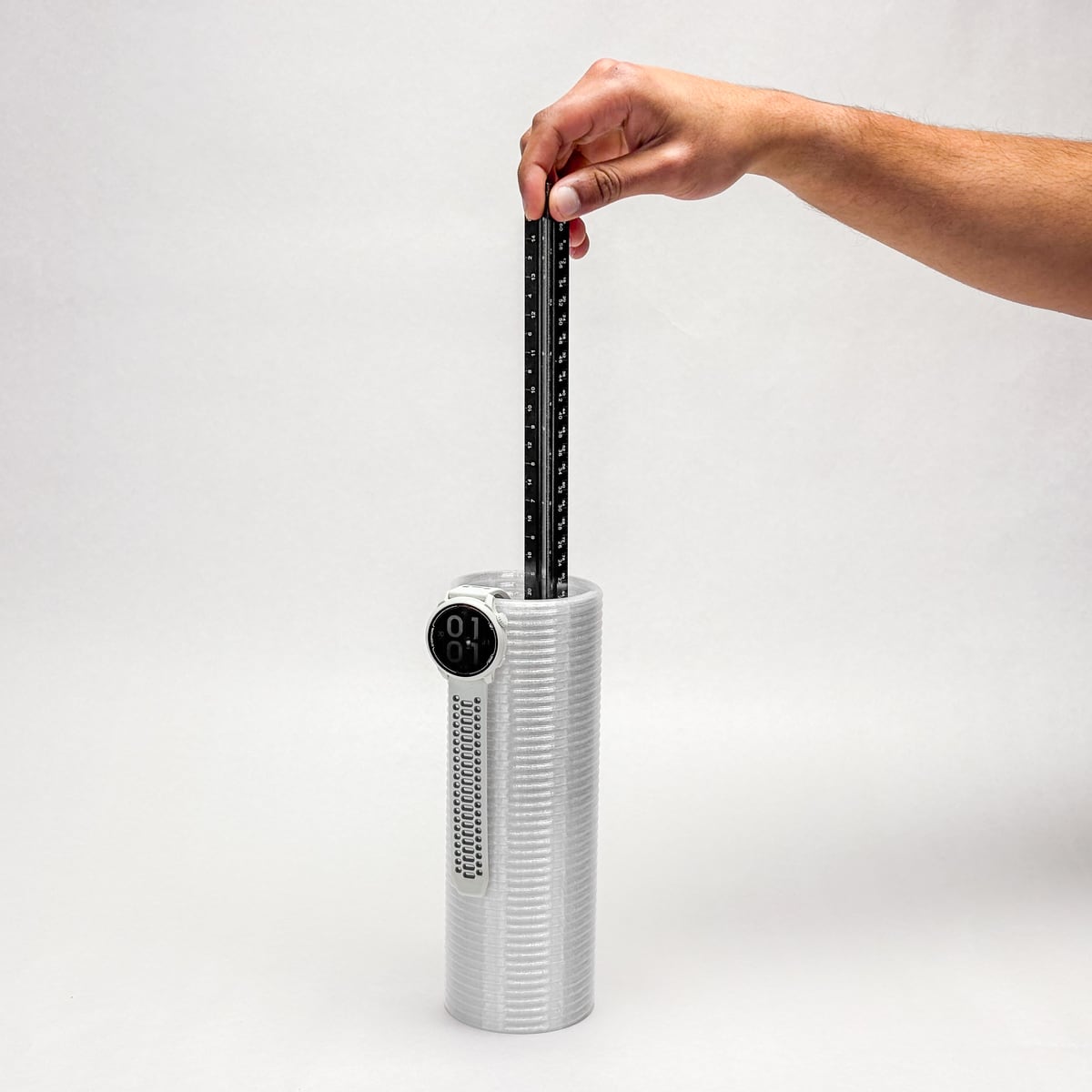 Hand pulling a black ruler-like slider from a white ribbed cylinder with a small round display on its front, white background