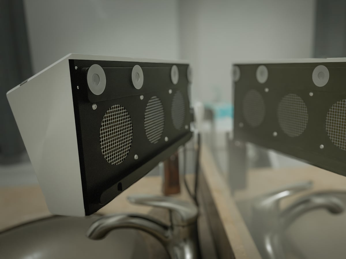Another angle of the white wedge defogger with black perforated face, reflected in the mirror above the sink