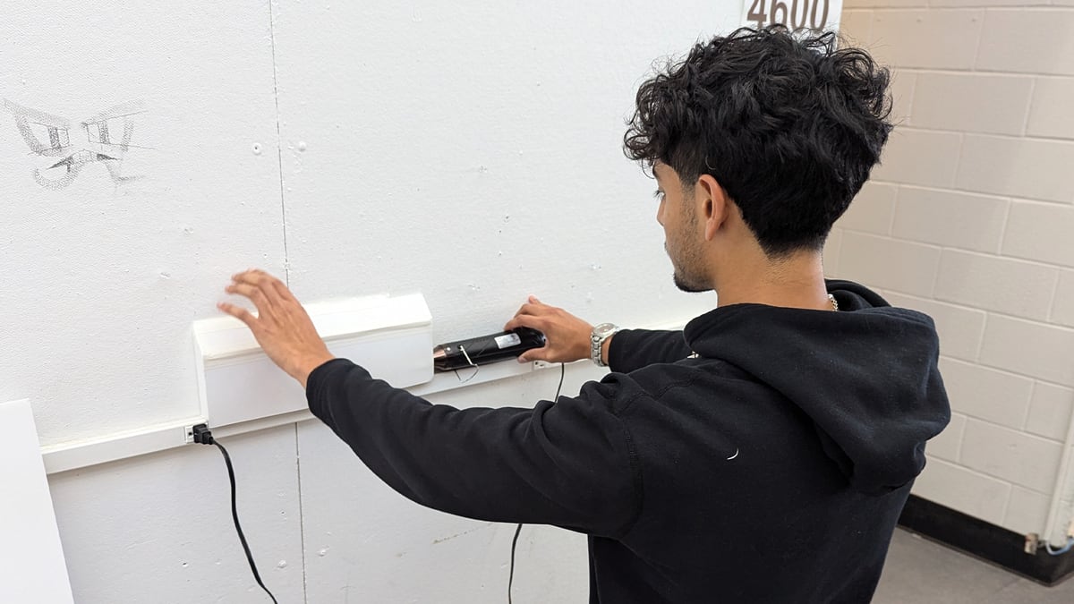 Photo of a young man with curly dark hair testing a prototype defogger on a white wall with a cable