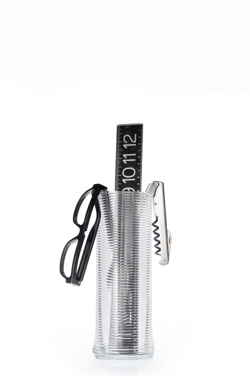 Ribbed glass vase used as a desk organizer holding glasses, a bottle opener and a black digit-marked clock bar