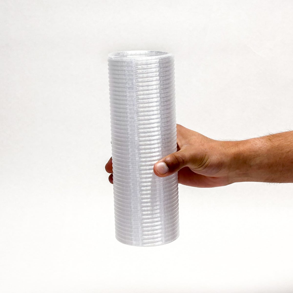 Hand holding a tall white ribbed cylinder against a white background