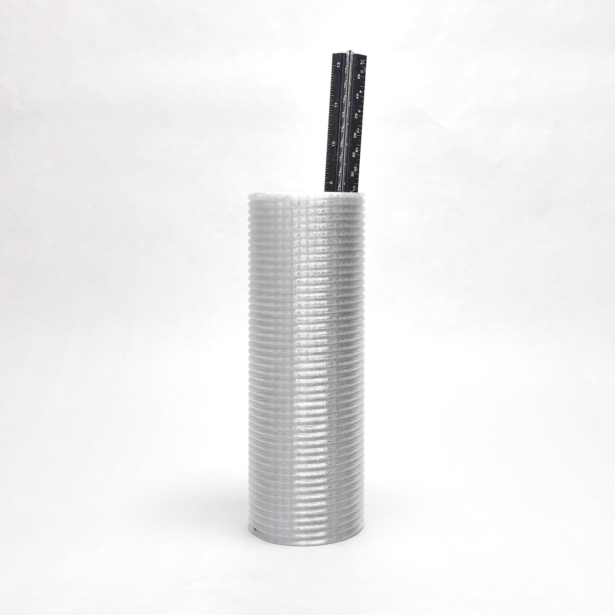 White ribbed cylinder with a black ruler-like insert sticking out the top, on a white background
