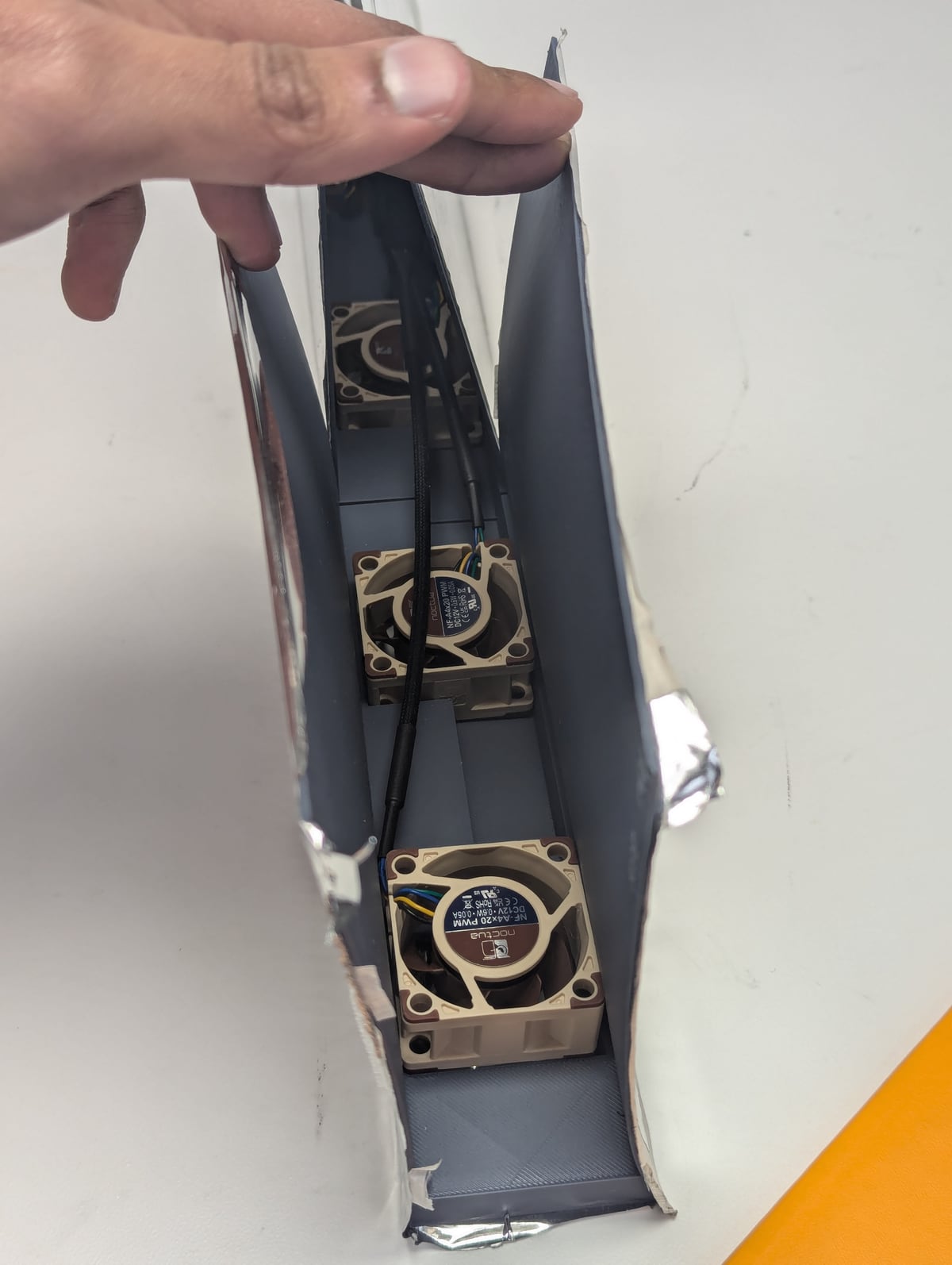 Hand holding open a slim grey box showing two small fans inside, white background