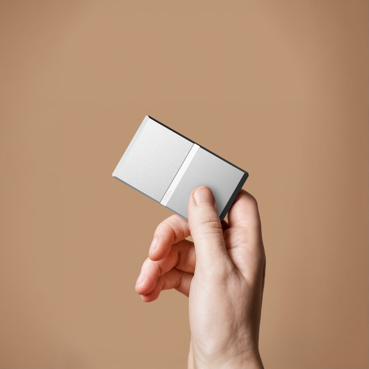 Hand holding a slim metal card-like device against tan background